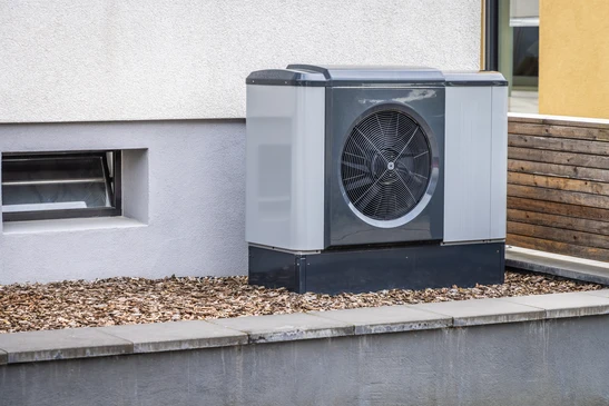Extérieur d'une maison moderne avec pompe à chaleur air-eau installée sur socle béton